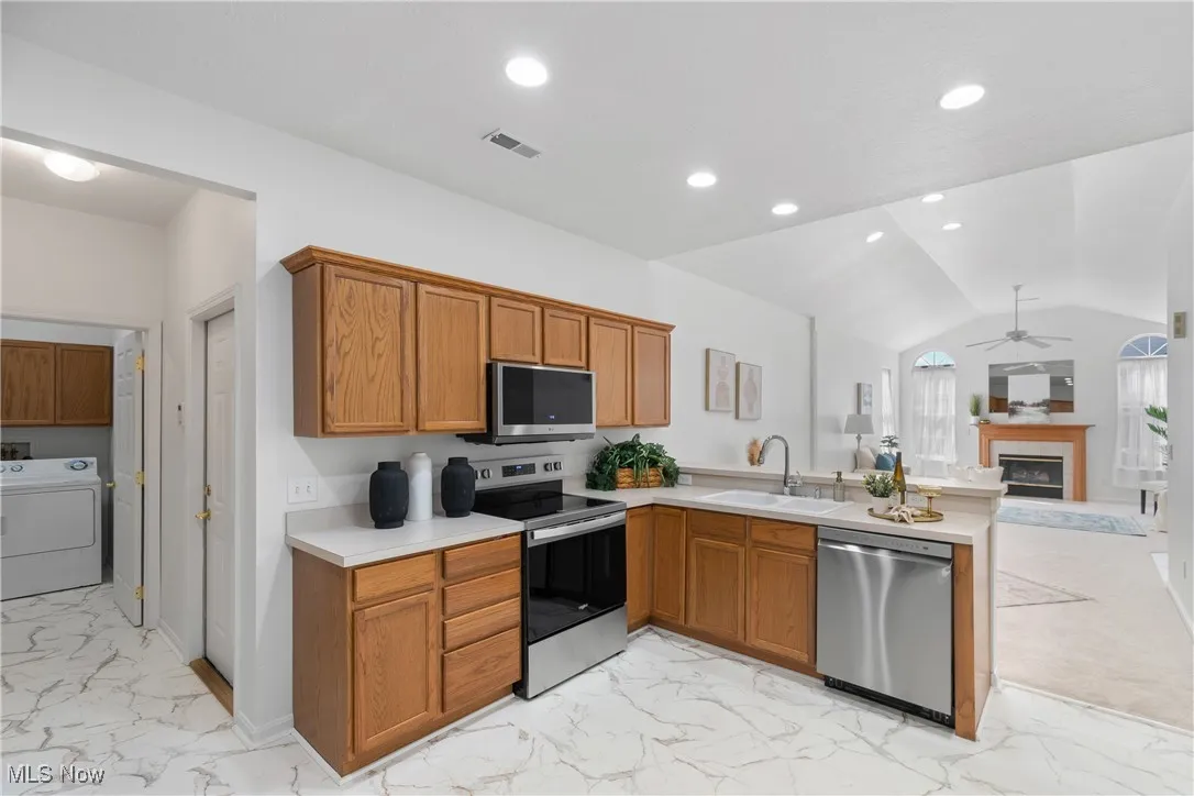 Kitchen with open floor plan, light marble finish flooring, a glass covered fireplace, appliances with stainless steel finishes, and recessed lighting