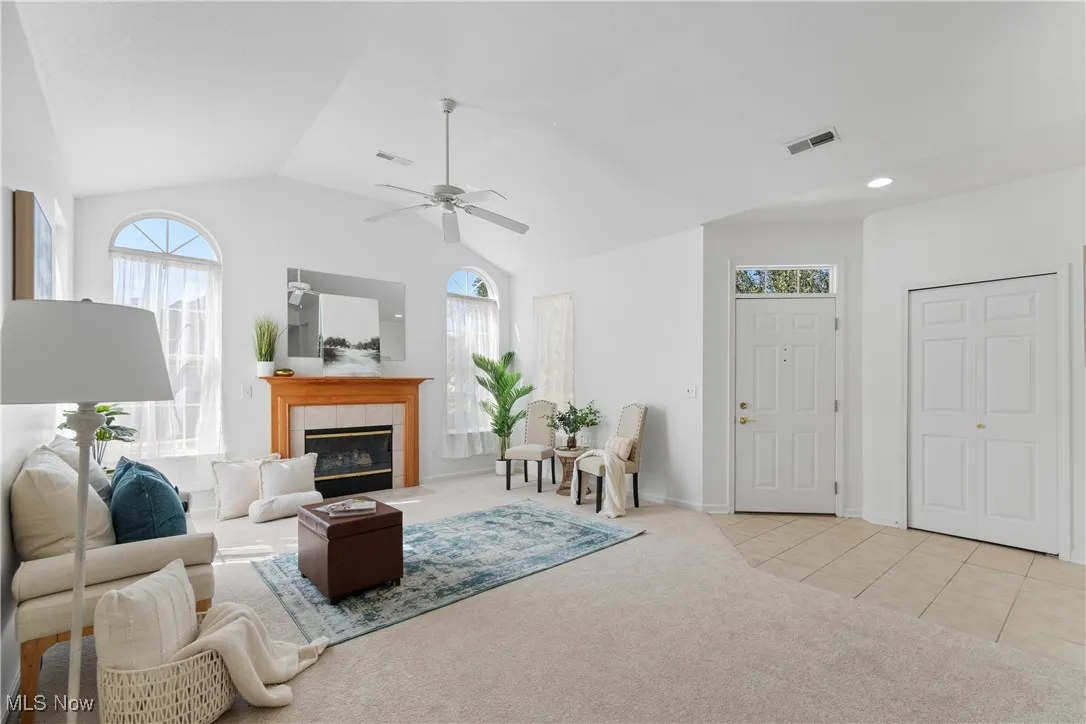 Living room with plenty of natural light, light carpet, lofted ceiling, a tiled fireplace, and light tile patterned floors