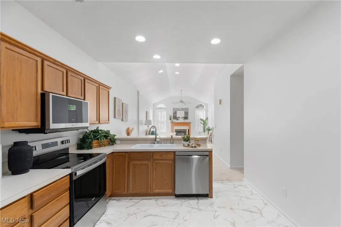 Kitchen with appliances with stainless steel finishes, light marble finish flooring, a fireplace, a ceiling fan, and light countertops
