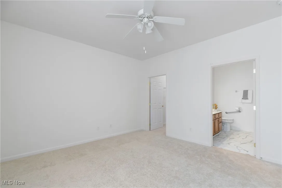 Unfurnished bedroom featuring light carpet, ensuite bathroom, and ceiling fan