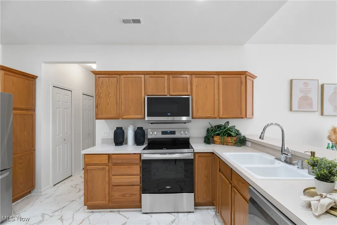 Kitchen featuring appliances with stainless steel finishes, brown cabinets, light countertops, and light marble finish floors