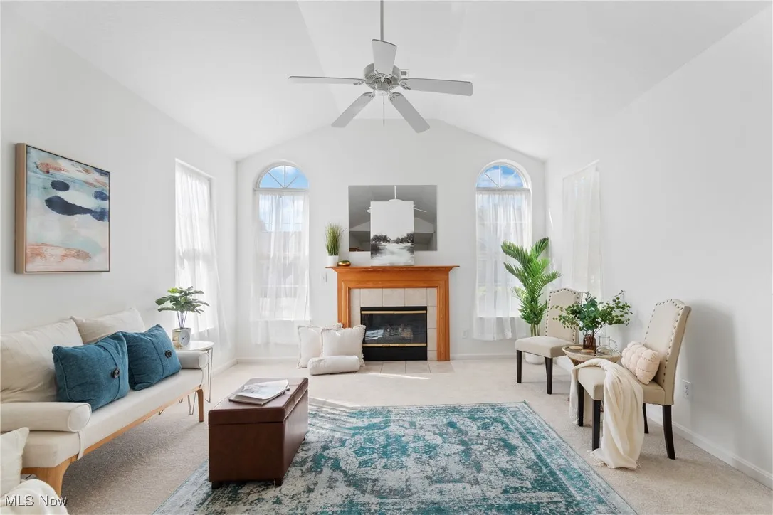 Living room featuring carpet flooring, vaulted ceiling, a fireplace, and ceiling fan