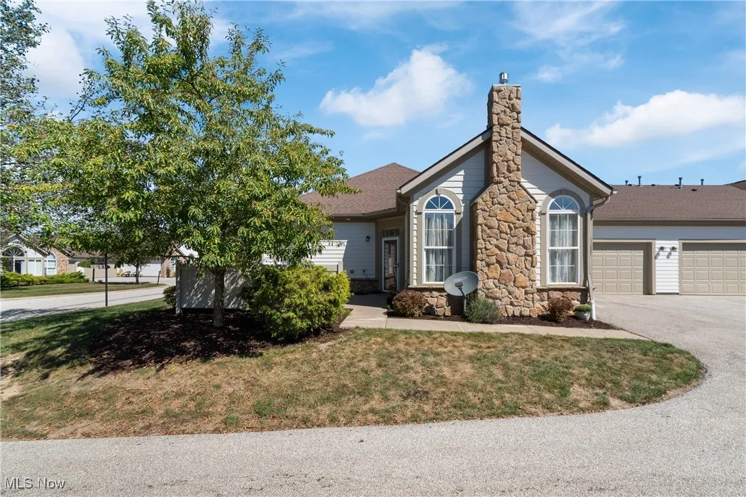 View of front of property with driveway, a garage, stone siding, a front lawn, and a chimney