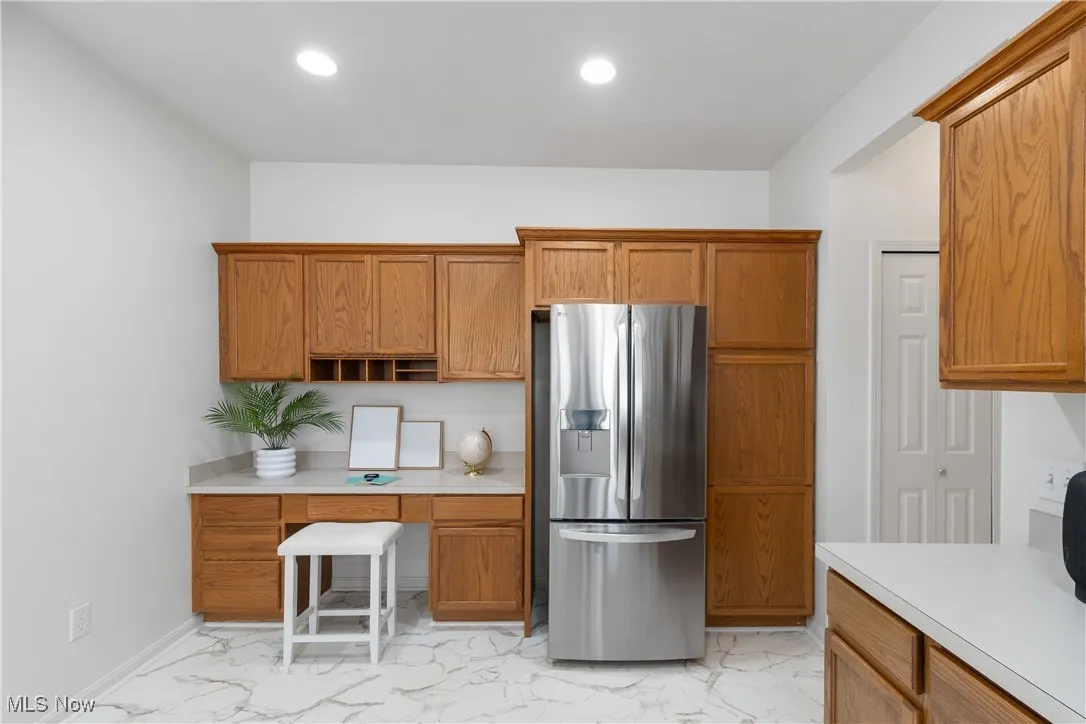 Kitchen featuring light marble finish floors, stainless steel fridge, brown cabinetry, light countertops, and recessed lighting