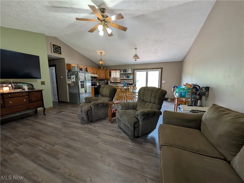 Living area with dark wood-style floors, vaulted ceiling, a textured ceiling, and a ceiling fan
