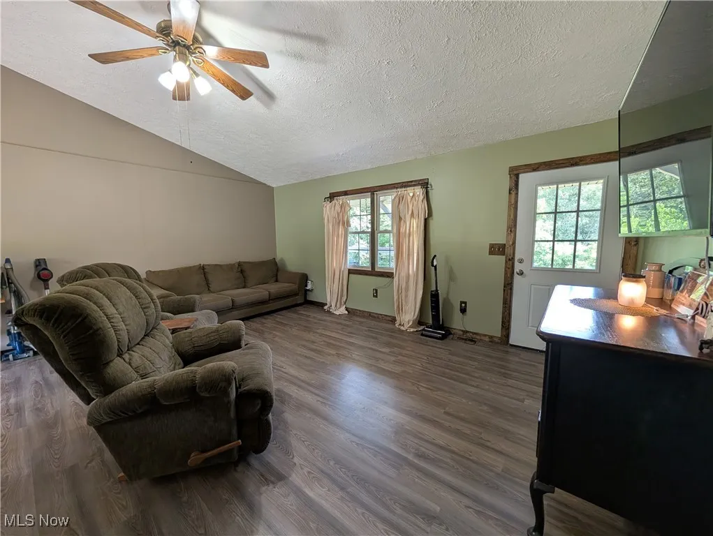 Living room featuring a textured ceiling, dark wood finished floors, lofted ceiling, and ceiling fan