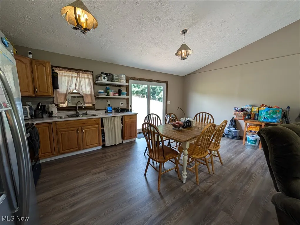 Dining room with dark wood-style floors, a textured ceiling, and vaulted ceiling