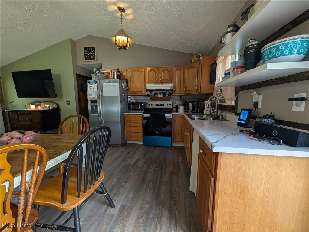Kitchen featuring light countertops, stainless steel appliances, dark wood-style flooring, brown cabinets, and pendant lighting