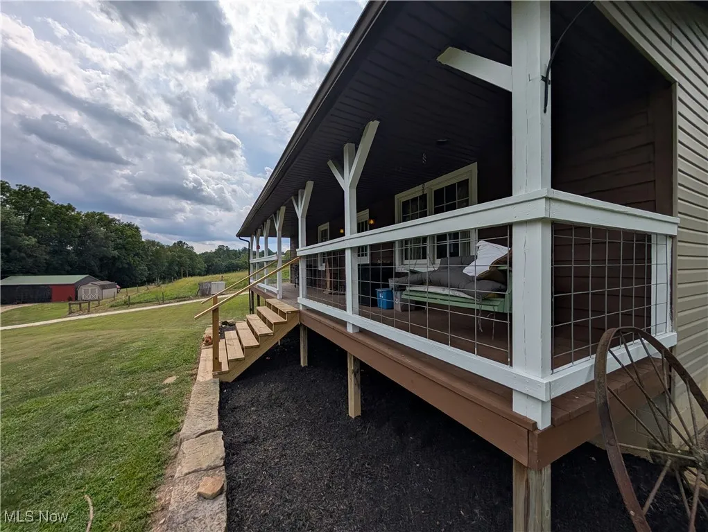 View of side of property featuring a yard, covered porch, and view of wooded area