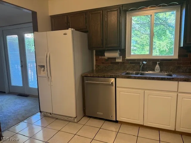 Kitchen featuring dark countertops, dishwasher, white fridge with ice dispenser, and light tile patterned floors