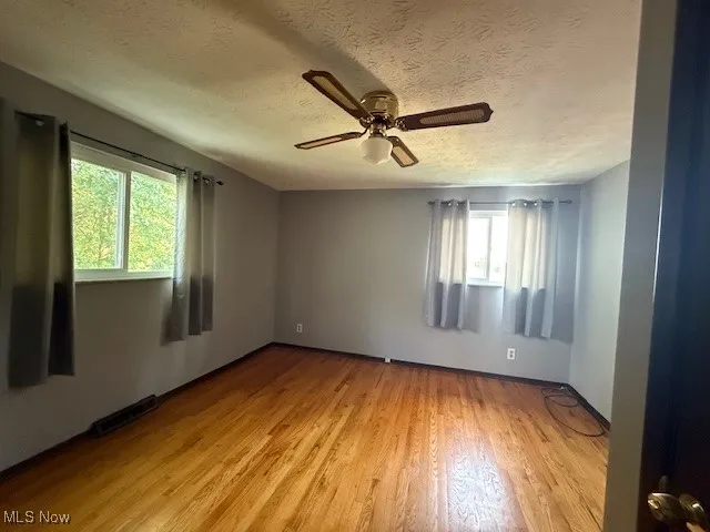 Primary bedroom featuring wood flooring, closets, a textured ceiling, and a lighted ceiling fan