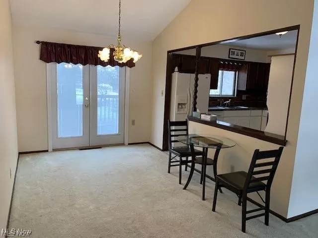 Kitchen with dark countertops, a breakfast bar, light colored carpet, lofted ceiling, and decorative light fixtures. French doors lead out to the deck.