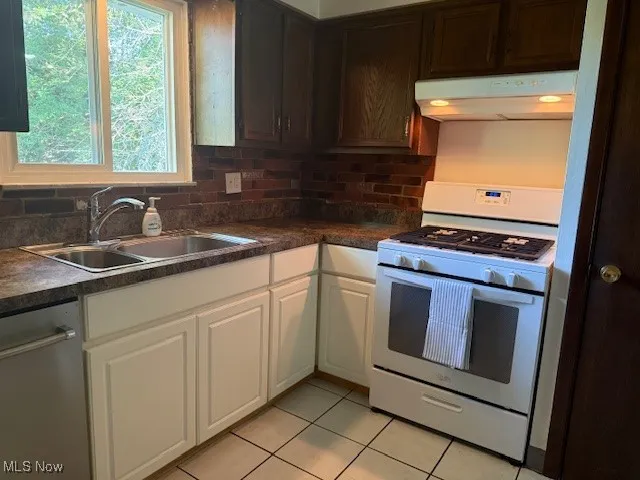 Kitchen with white range with gas cooktop, dark countertops, stainless steel dishwasher, and under cabinet range hood