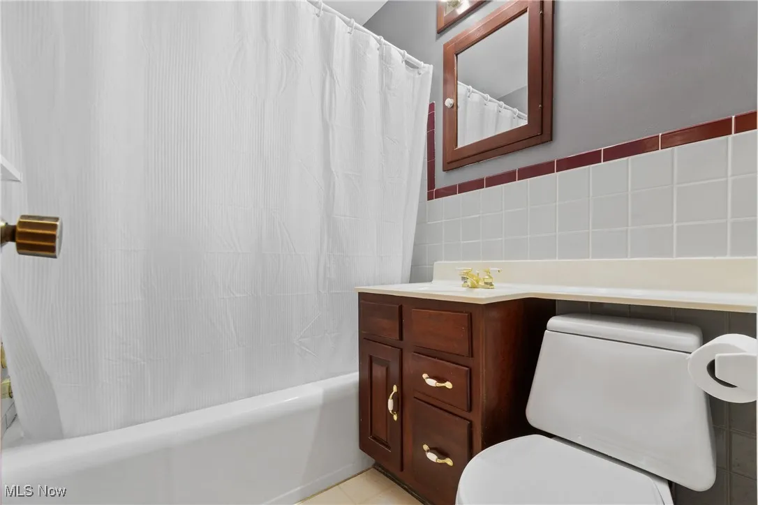 Full bath featuring tile walls, shower / bath combo with shower curtain, vanity, and light tile patterned flooring