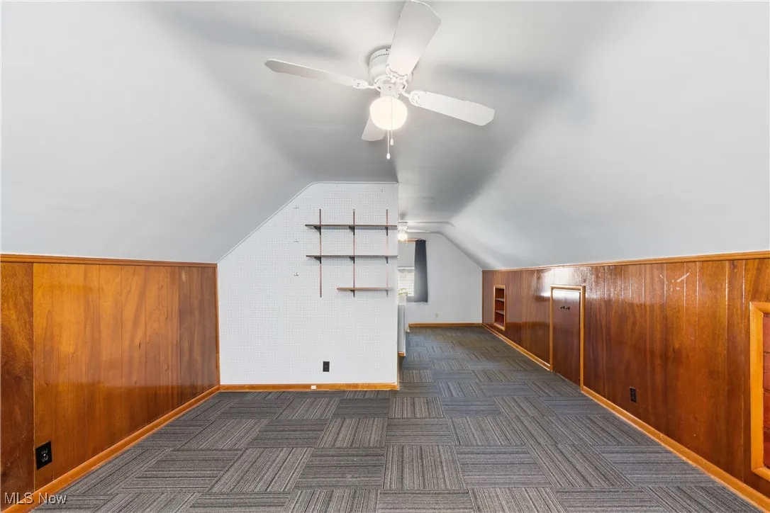 Bonus room with wood walls, vaulted ceiling, dark carpet, and ceiling fan