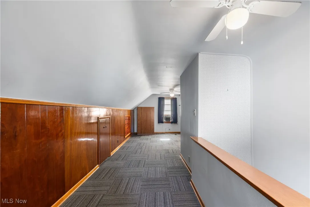Hallway featuring wood walls, vaulted ceiling, and dark carpet