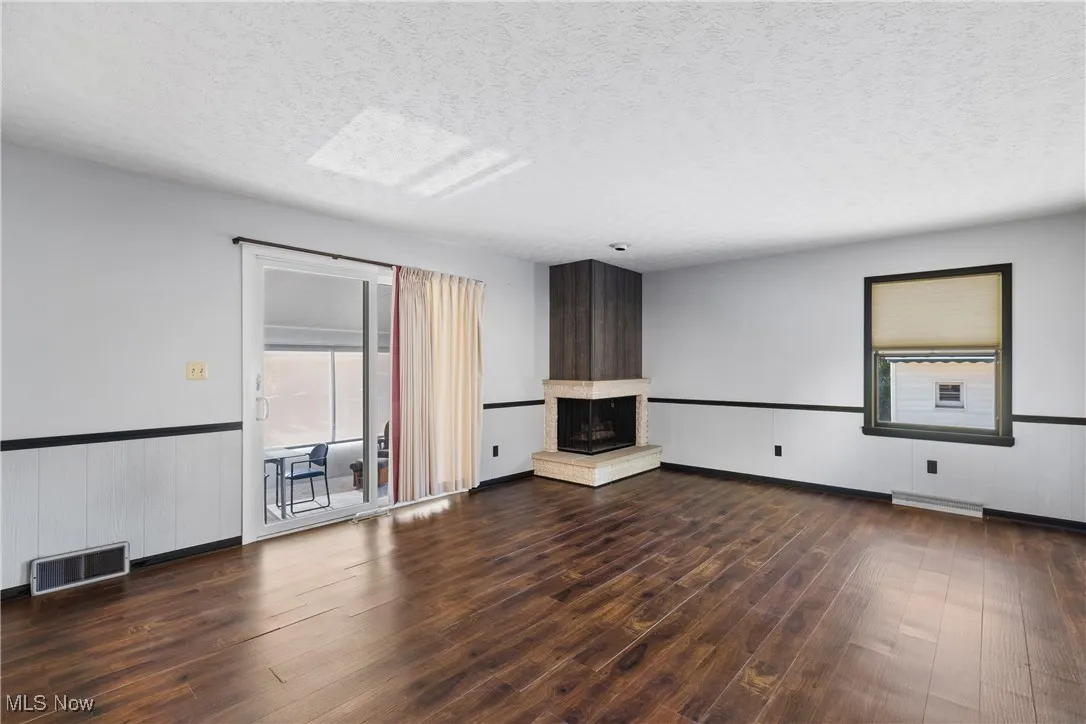 Unfurnished living room featuring a wainscoted wall, a textured ceiling, dark wood-style floors, and a fireplace