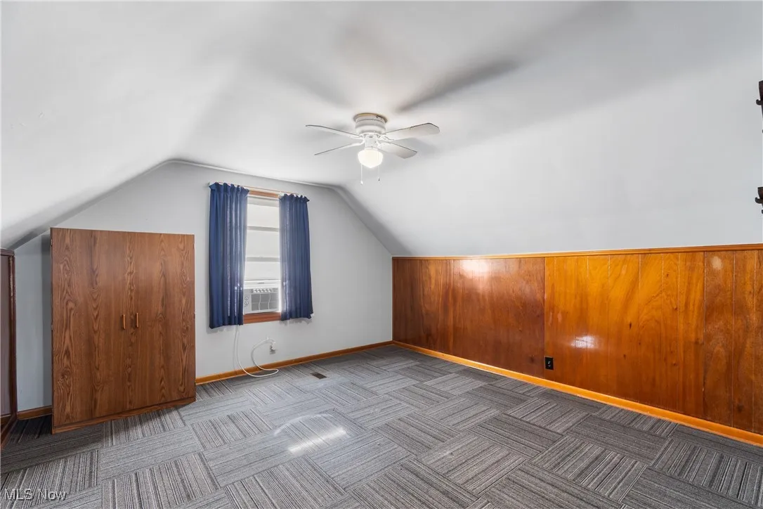 Bonus room with lofted ceiling, wood walls, ceiling fan, and carpet flooring