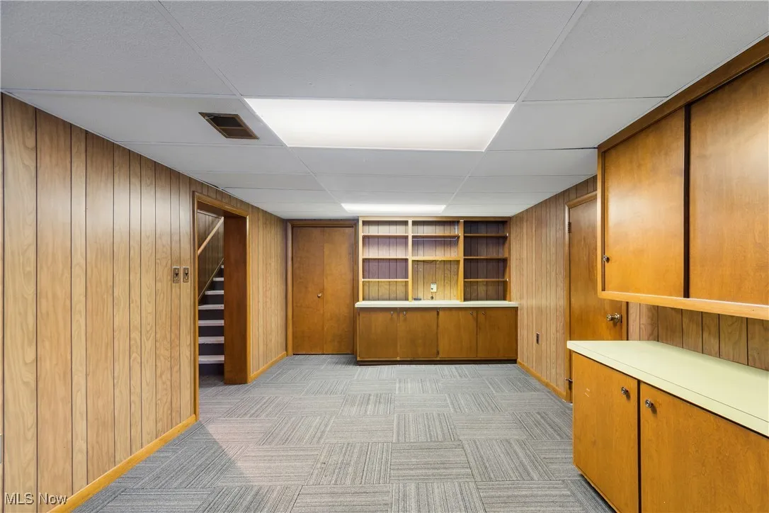 Finished below grade area featuring a drop ceiling, wooden walls, stairway, and light carpet