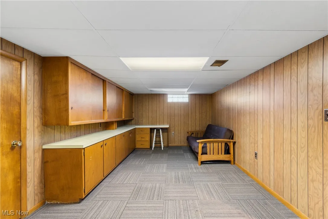 Rec Room area with a drop ceiling, light countertops, wooden walls, brown cabinets, and light carpet