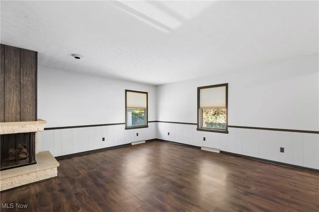 Unfurnished living room featuring a fireplace, dark wood finished floors, wainscoting, and a textured ceiling