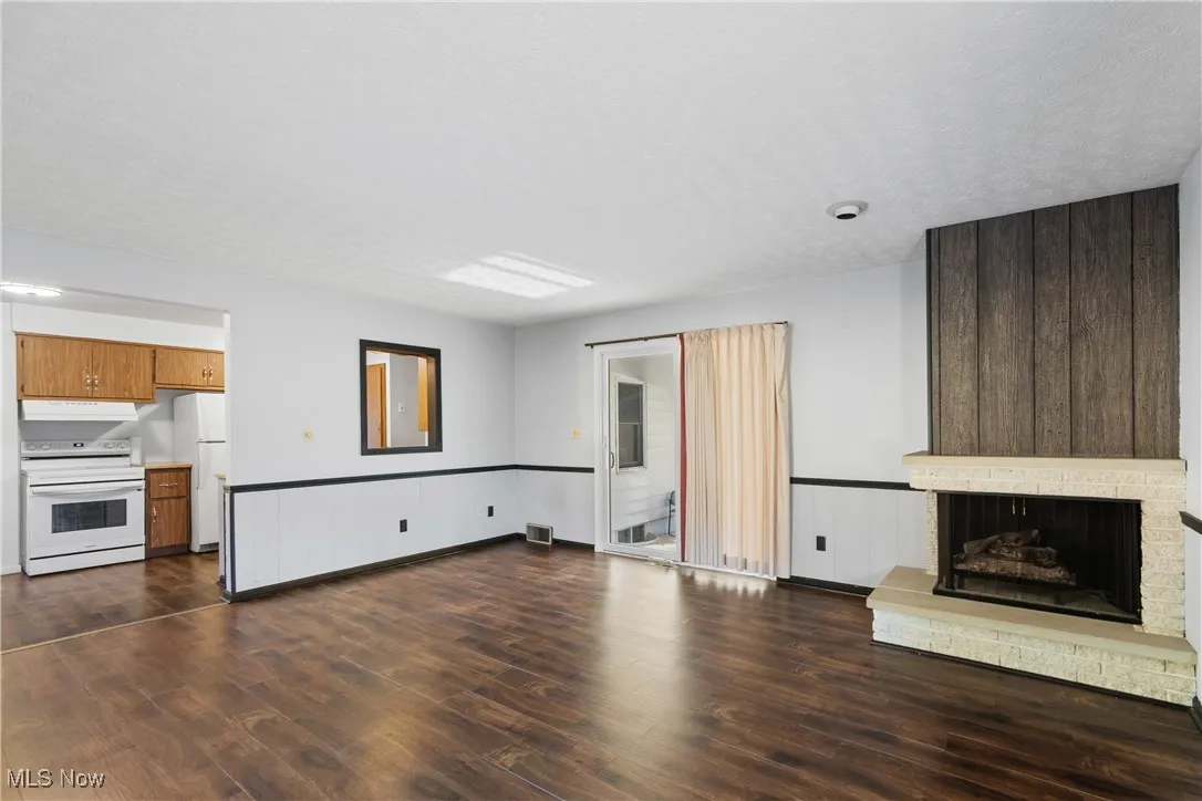 Unfurnished living room with dark wood-style flooring, a brick fireplace, and a wainscoted wall
