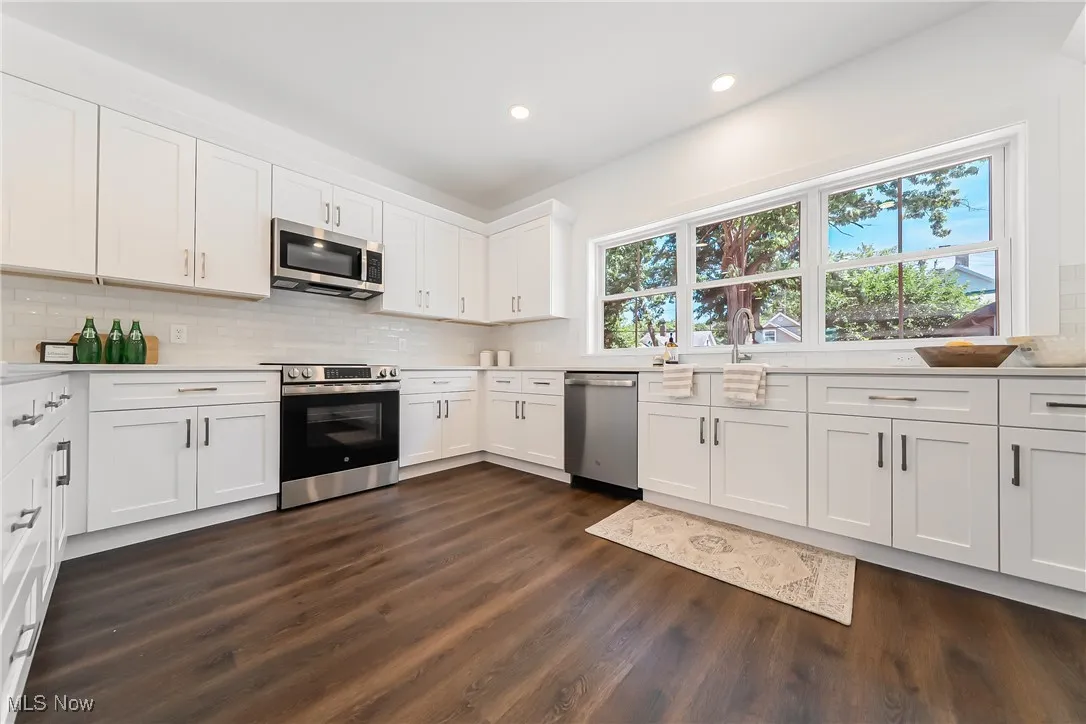 Kitchen with backsplash, white cabinets, stainless steel appliances, recessed lighting, and dark wood-style flooring
