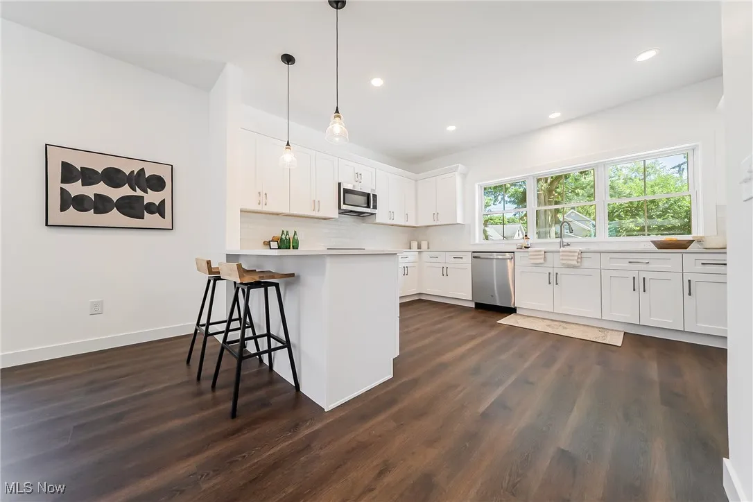 Kitchen featuring light countertops, decorative light fixtures, dark wood-style flooring, a breakfast bar, and white cabinets