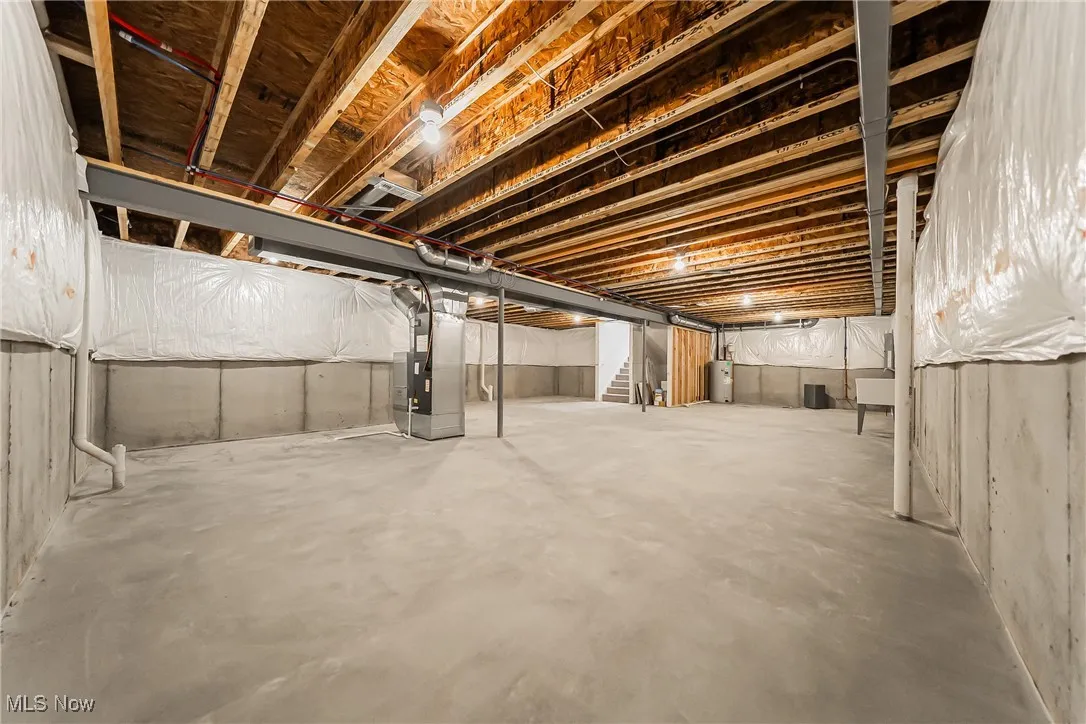 Unfinished basement with stairs, heating unit, and water heater