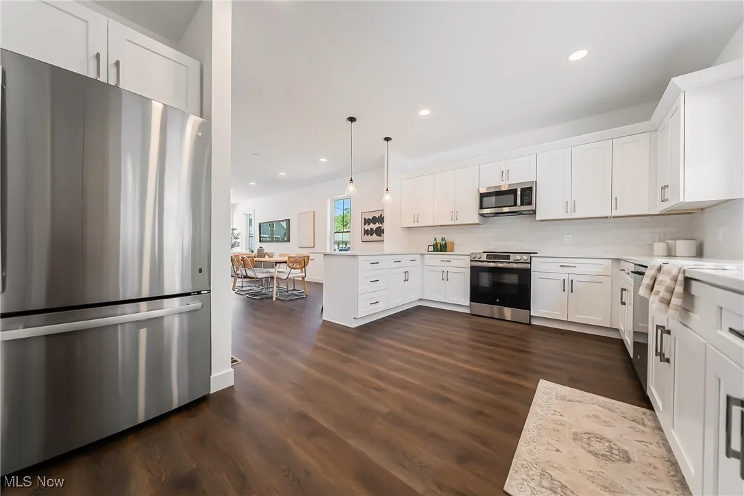 Kitchen with appliances with stainless steel finishes, white cabinetry, open floor plan, decorative light fixtures, and tasteful backsplash