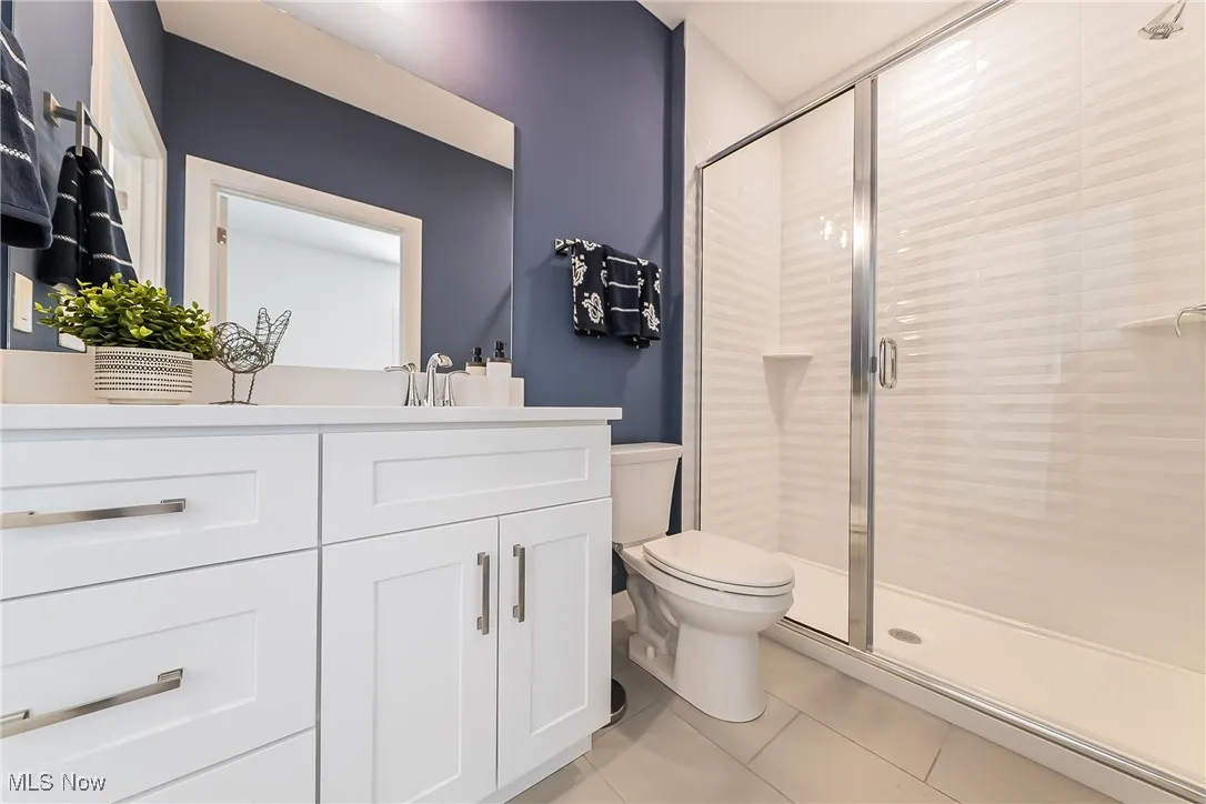 Bathroom featuring a shower stall, vanity, and light tile floors