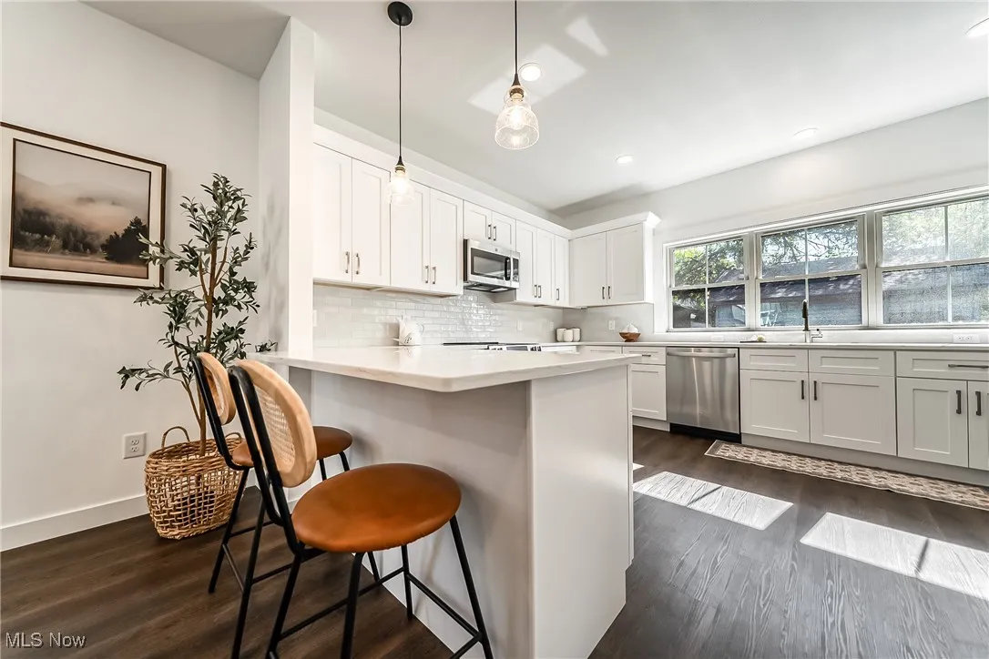 Kitchen with dark wood-style flooring, pendant lighting, a breakfast bar, decorative backsplash, and recessed lighting