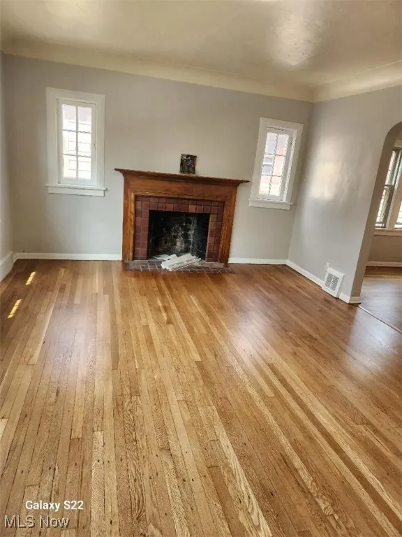 Unfurnished living room featuring arched walkways, a fireplace, light wood-type flooring, and healthy amount of natural light