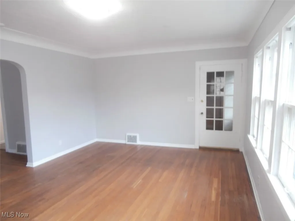 Unfurnished room featuring arched walkways, dark wood-type flooring, and ornamental molding