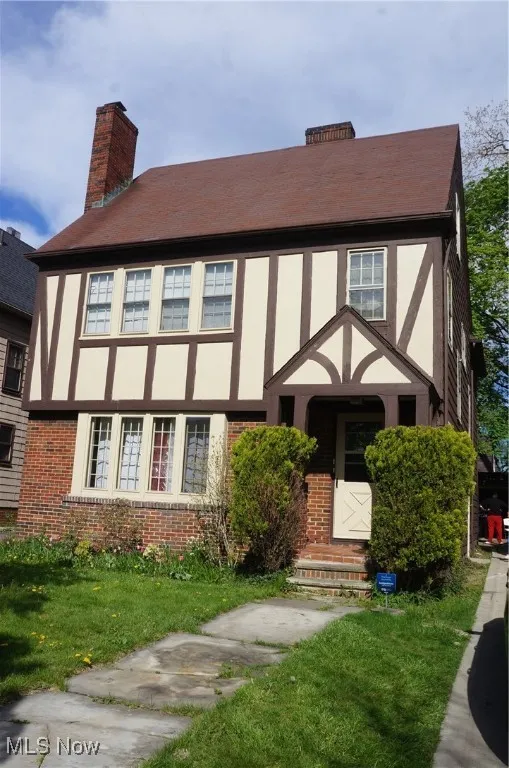 View of front facade featuring a chimney, brick siding, and a front lawn