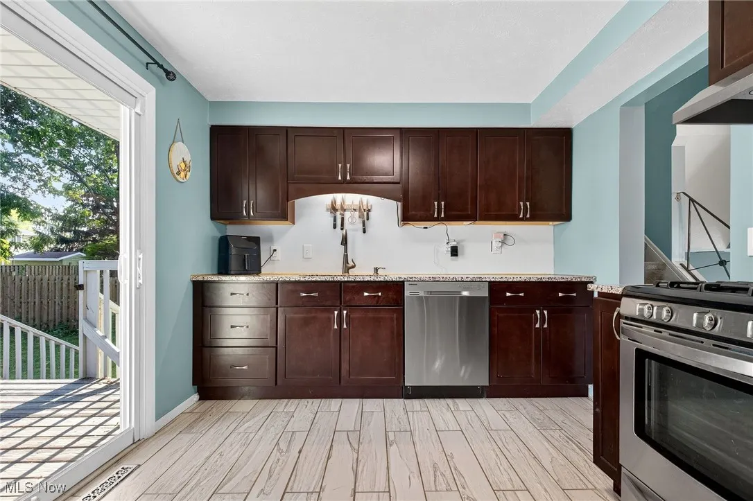 Kitchen with stainless steel appliances, dark brown cabinetry, wood tiled floors, and light stone countertops