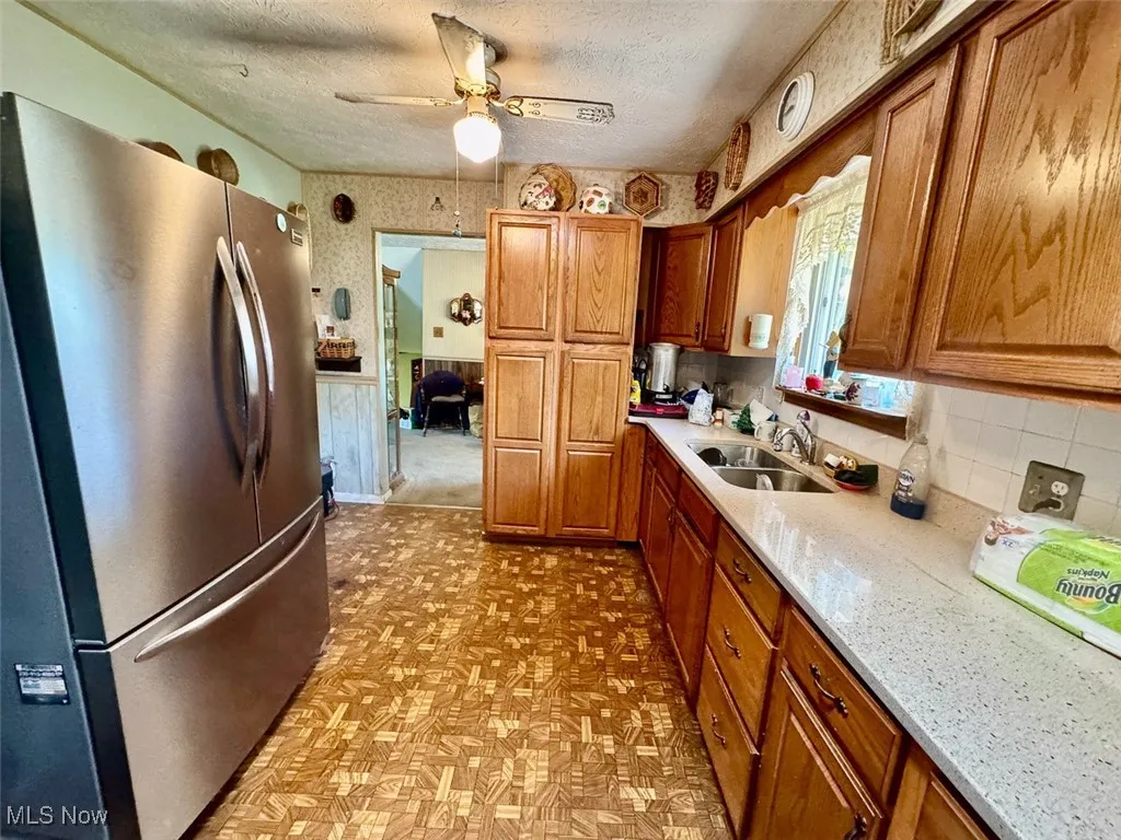Kitchen with freestanding refrigerator, brown cabinets, a ceiling fan, light stone counters, and a textured ceiling