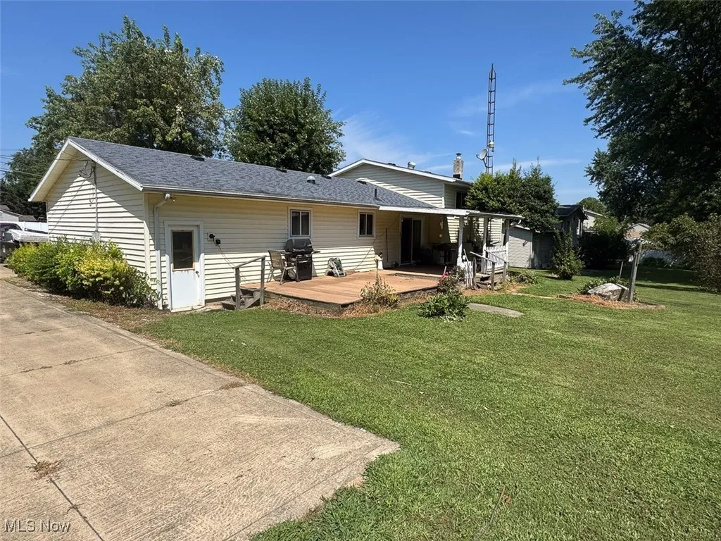 Rear view of property with a deck, a yard, and a shingled roof