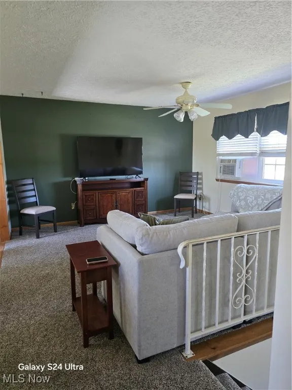 Living area featuring a textured ceiling, carpet, and ceiling fan