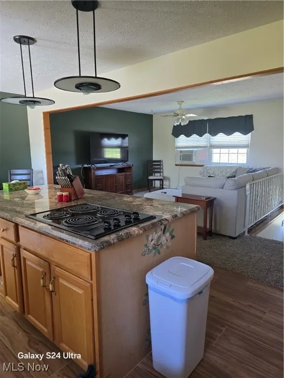 Kitchen featuring open floor plan, decorative light fixtures, a textured ceiling, dark wood-style floors, and stovetop
