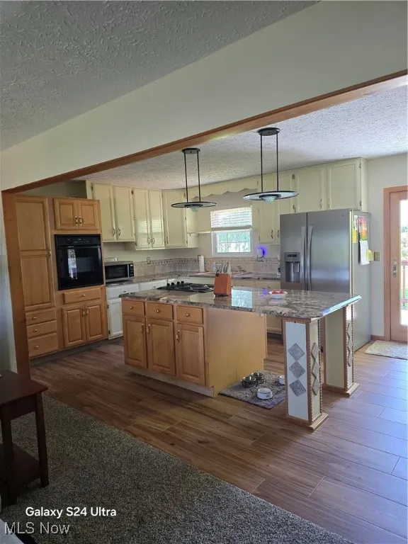 Kitchen featuring pendant lighting, a kitchen island, a textured ceiling, dark stone countertops, and fridge