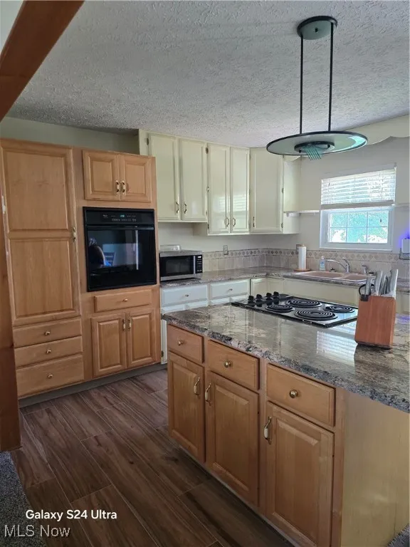 Kitchen featuring a textured ceiling, dark wood-type flooring, oven, dark stone counters, and cooktop