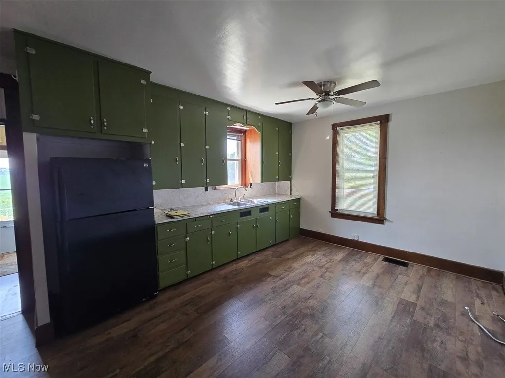 Kitchen with green cabinetry, light countertops, freestanding refrigerator, dark wood-type flooring, and a ceiling fan