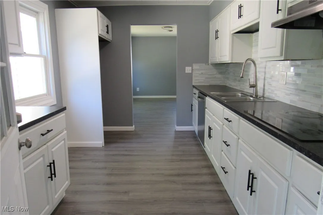 Kitchen with dark countertops, under cabinet range hood, white cabinets, and black electric stovetop