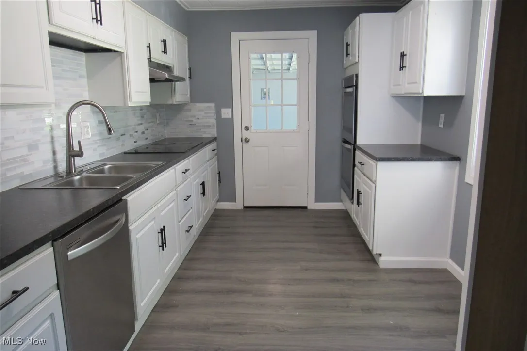 Kitchen with tasteful backsplash, appliances with stainless steel finishes, white cabinets, and ornamental molding