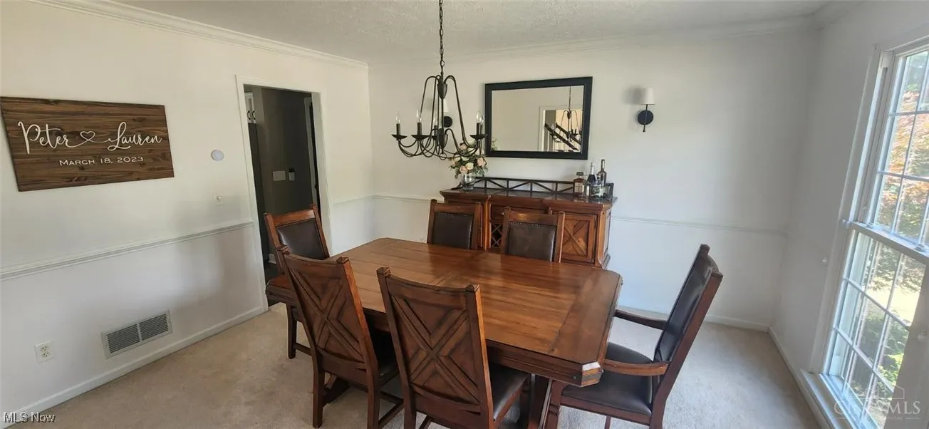 Dining room featuring ornamental molding, light carpet, a textured ceiling, and a chandelier