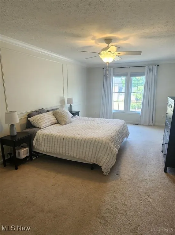 Bedroom with light carpet, a textured ceiling, a ceiling fan, and crown molding