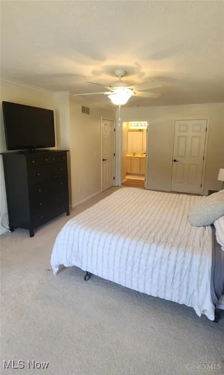 Carpeted bedroom with ornamental molding, a textured ceiling, ensuite bath, and ceiling fan