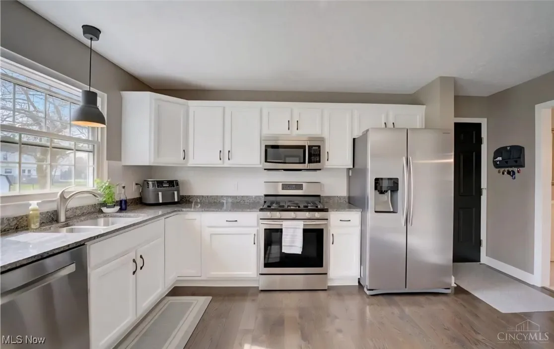 Kitchen with stainless steel appliances, light stone counters, white cabinetry, light wood-type flooring, and pendant lighting