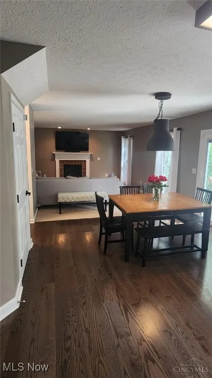 Dining space with dark wood-style flooring, a fireplace, and a textured ceiling